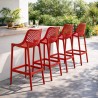 Lot de 4 tabourets de jardin BROZER rouges en plastique, installés autour d’un bar extérieur moderne